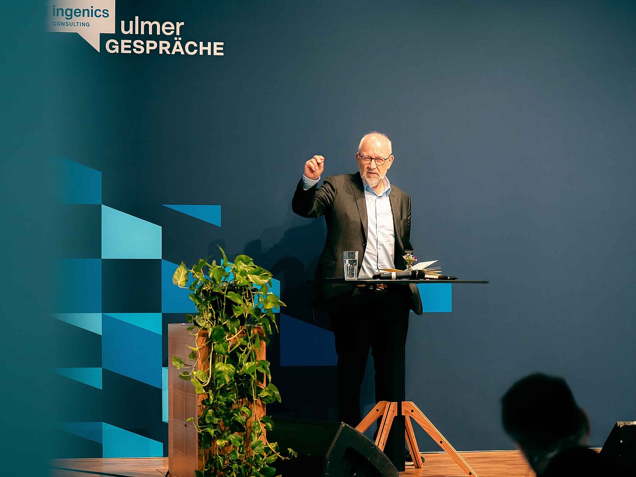 Redner auf einer Bühne mit Stehtisch während eines Vortrags bei den Ulmer Gesprächen