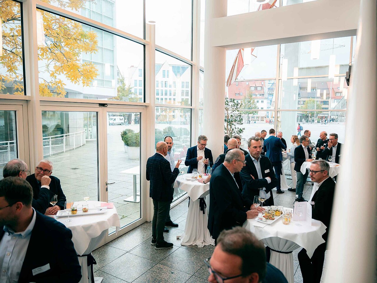Teilnehmende einer Fachveranstaltung tauschen sich bei einem Stehempfang in einem lichtdurchfluteten Foyer aus