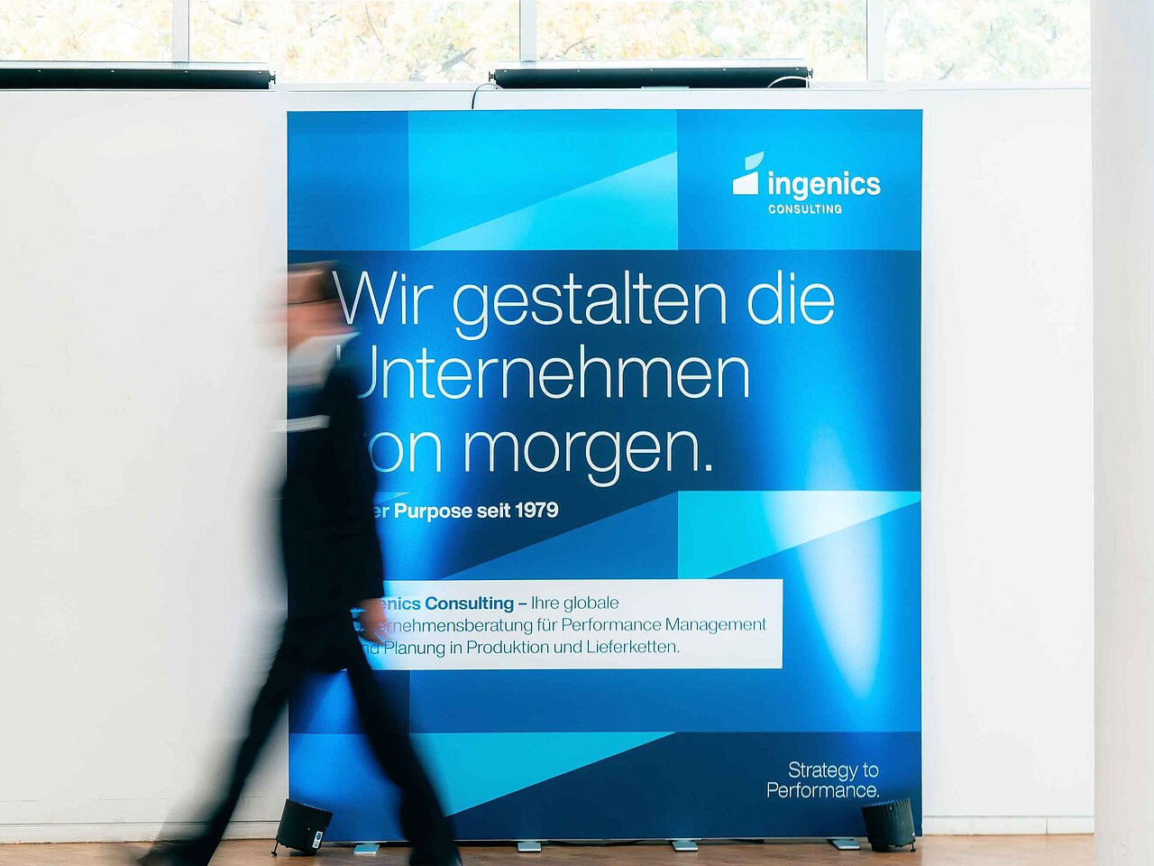 Person geht an einer Ingenics Markenwand mit Unternehmensleitbild vorbei