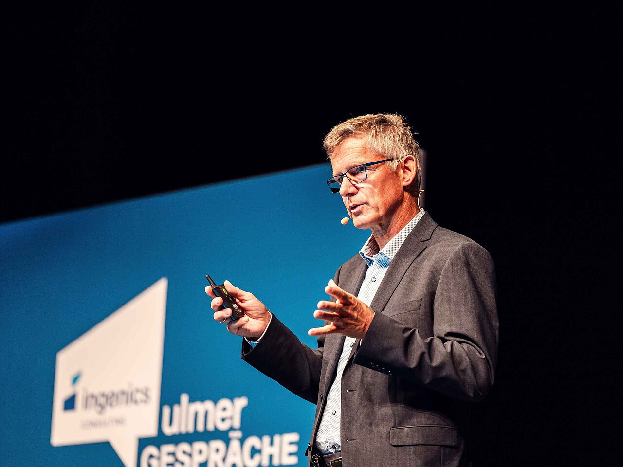 Referierende Person hält einen Vortrag auf der Bühne der Ulmer Gespräche vor einer Präsentationswand