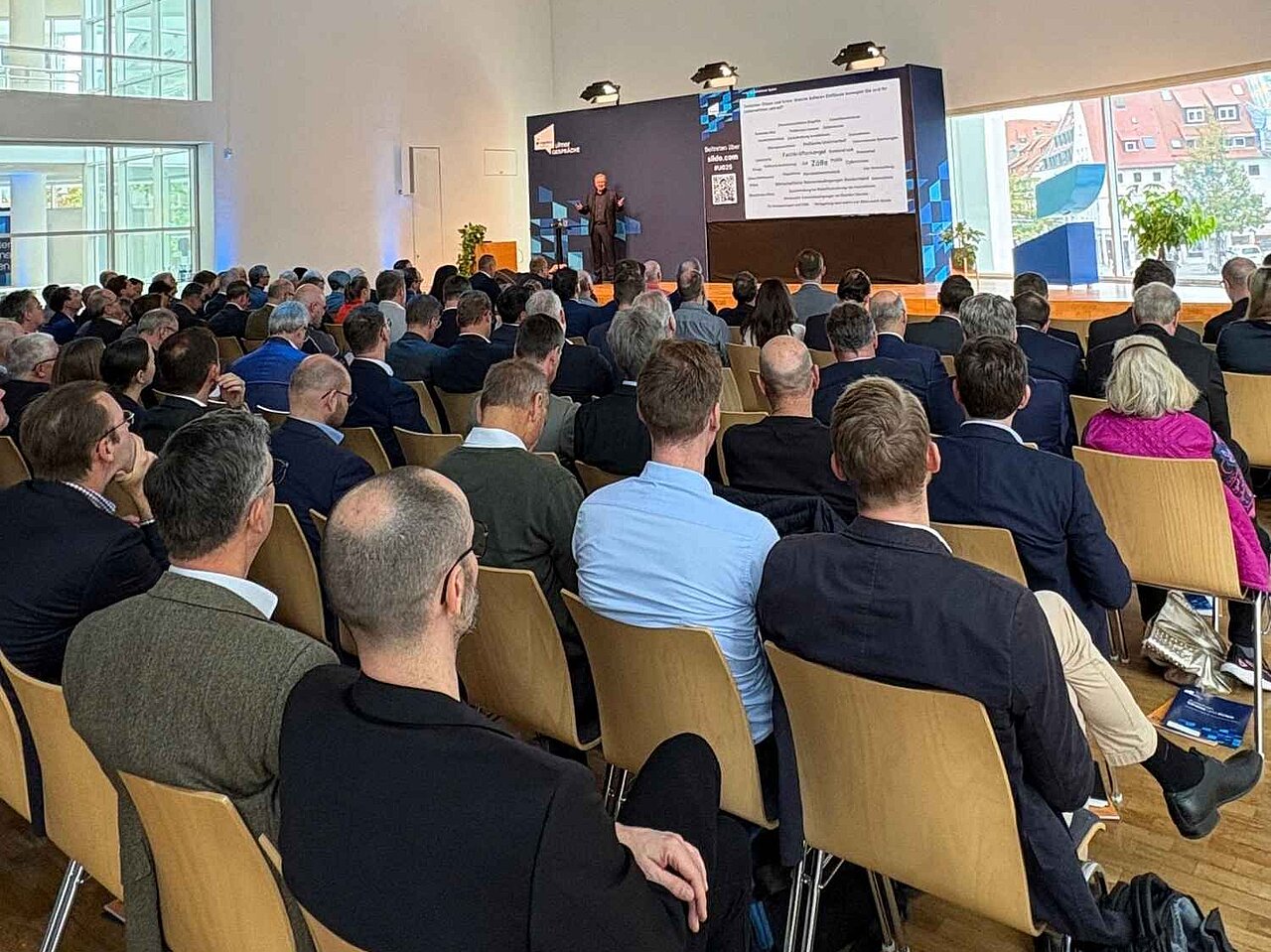 Teilnehmende verfolgen einen Vortrag in einem voll besetzten Veranstaltungssaal