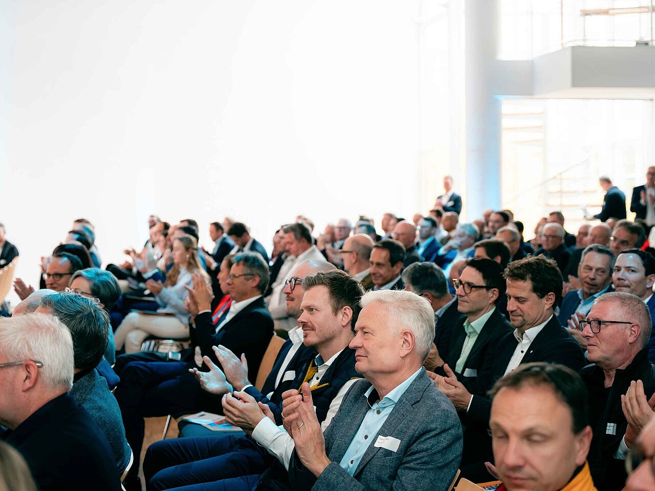 Teilnehmende einer Fachveranstaltung sitzen im Publikum und applaudieren nach einem Vortrag